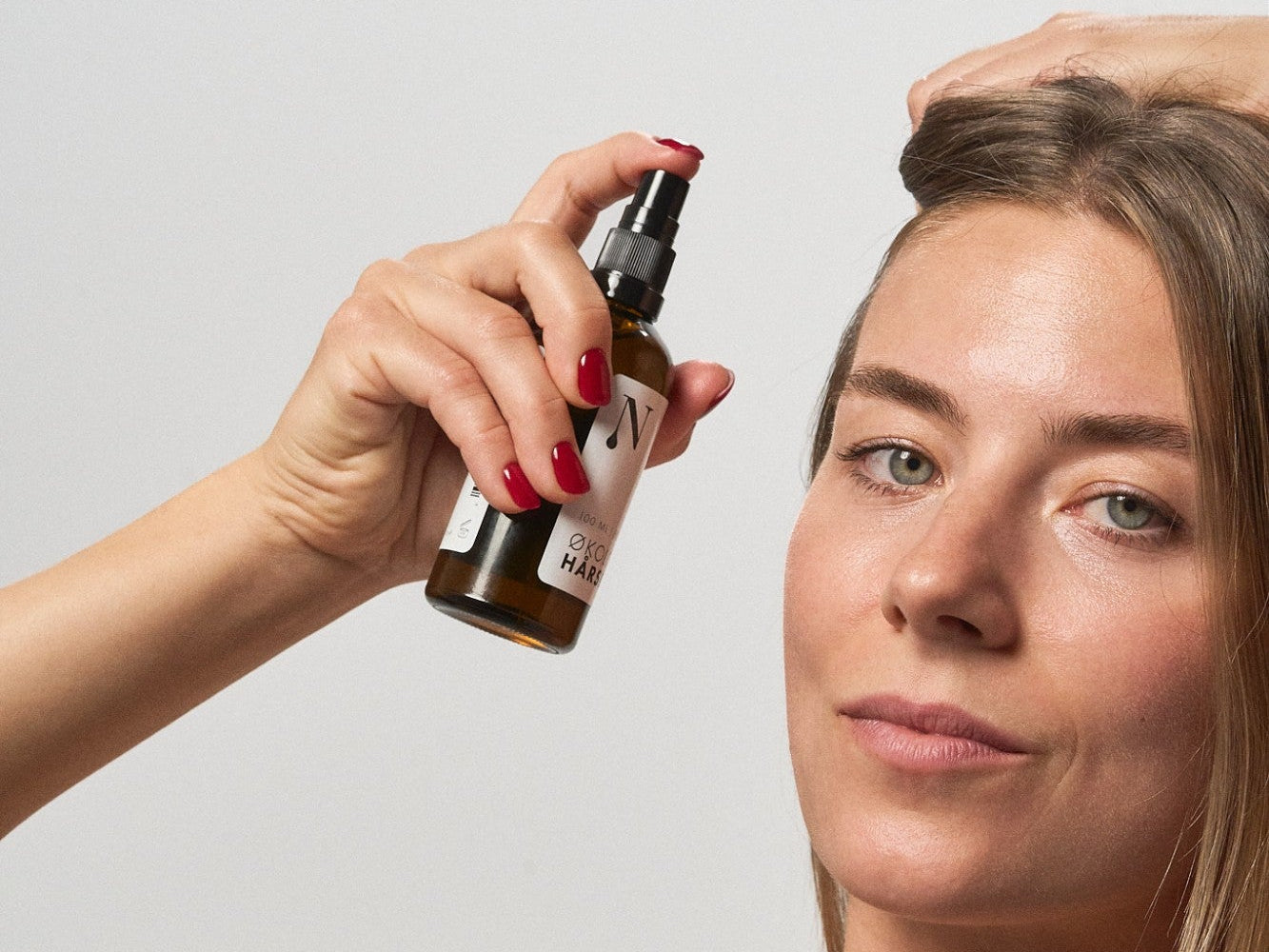 Kvinde sprayer Hårserum fra Naturligolie i hovedbunden med den ene hånd i håret.